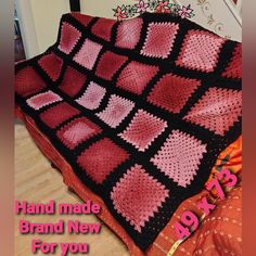 a pink and black crocheted blanket sitting on top of a bed next to a pillow