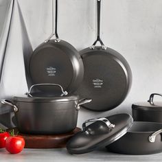 an assortment of pots and pans hanging from hooks on a wall next to tomatoes