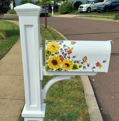 a white mailbox with sunflowers painted on it's side next to a sidewalk