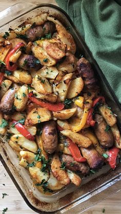 a casserole dish filled with potatoes, peppers and sausages on a wooden table