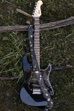 Black vine guitar strap. Printed with vines and white flowers on black background. Attached to black electric guitar laying on grass and logs Aesthetic Electric Guitar, National Park Patches, Mountain Tree, Black Electric Guitar, Unique Guitars, Guitar Straps