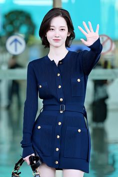 a woman in a short blue dress waves to the crowd while holding her hand up