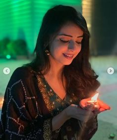 a woman holding a lit candle in her hand and looking at the screen on her phone