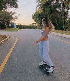 a woman riding a skateboard down the middle of a street in front of trees