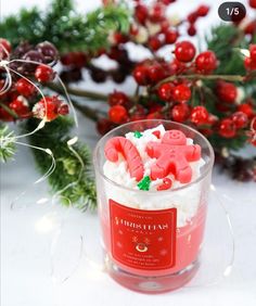 a candle that is sitting in front of some christmas wreaths and holly branches with red berries around it