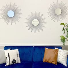 three sunburst mirrors mounted on the wall above a blue couch with decorative pillows