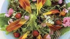 a blue plate topped with salad covered in orange and pink flower petals next to a fork