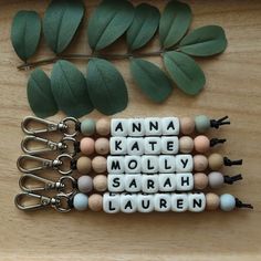 four keychains with words written on them sitting next to some green leafy branches