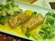 two fish fillets on a white plate with potatoes and cucumber garnish