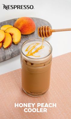 a jar of honey peach cooler sitting on top of a table next to sliced peaches