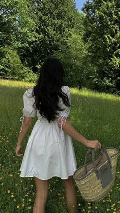 a woman in a white dress is walking through the grass with a wicker basket