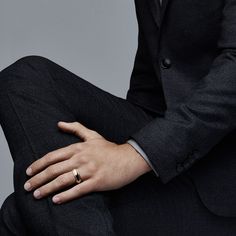 a man in a suit and tie sitting down with his hand on his lapel