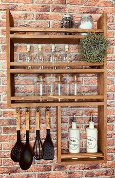 an old wooden shelf with utensils and bottles on it against a brick wall