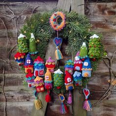 a christmas wreath hanging on the side of a wooden fence with knitted ornaments around it