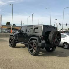 a black jeep parked in a parking lot next to a white car with red rims