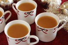 four white mugs filled with brown liquid on top of a red cloth covered table