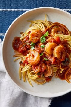 pasta with shrimp and tomato sauce in a white bowl on top of a blue table cloth