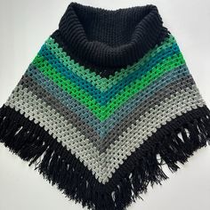 a crocheted ponchle with fringes on the bottom and green, white, black and grey colors