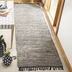 a rug with tassels on the floor next to two vases and a potted plant