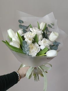 a person holding a bouquet of white flowers with greenery on the stems and leaves