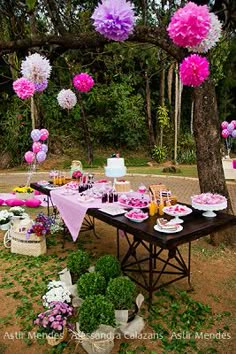 a table set up for a party with pink and white flowers hanging from the trees