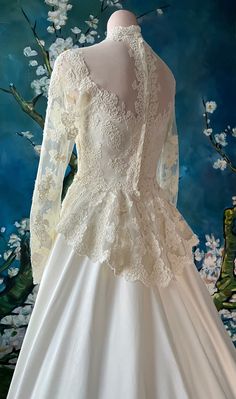 a white wedding dress on display in front of a wall with flowers and branches behind it