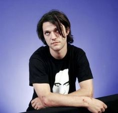 a young man with long hair sitting on a black table and looking at the camera