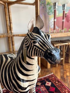 a zebra statue sitting on top of a wooden floor next to a rug and chair