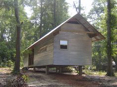 a small wooden cabin in the middle of some trees and dirt area with no people around it