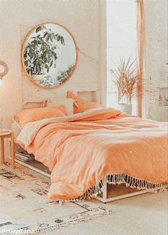 a bed with orange sheets and pillows in a room next to a round mirror on the wall