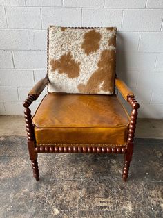 a brown and white cowhide chair with wooden legs on concrete floor next to brick wall