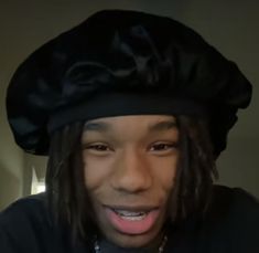 a man with dreadlocks wearing a black hat and making a funny face while looking at the camera