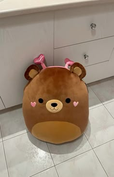 a brown teddy bear pillow sitting on top of a kitchen floor