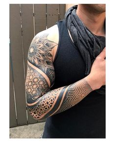 a man with a tattoo on his arm and shoulder is standing in front of a wall