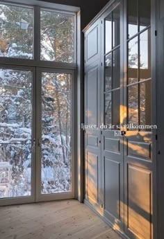 an empty room with glass doors and snow covered trees in the background on a sunny day