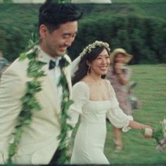 a bride and groom are walking through the grass with leis around their necks as they smile at each other