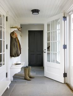 an entryway with white walls and wooden doors, two coats hanging on hooks, and boots