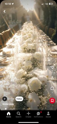 a long table with white flowers and place settings on the phone screen is seen in this image