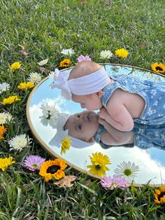 a baby looking at its reflection in a mirror with daisies on the ground next to it