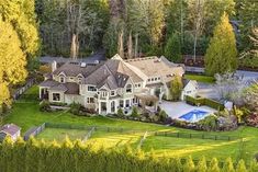 an aerial view of a large home surrounded by trees and grass with a swimming pool in the foreground