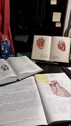 an open book sitting on top of a table next to two books with human heart diagrams