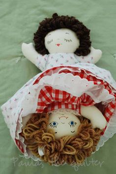 two dolls laying on top of each other in a basket with red and white fabric