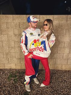 a man and woman dressed up in racing gear standing next to a brick wall with the words worlde written on it