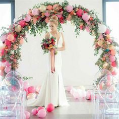 a woman standing in front of a pink and white arch with balloons on the floor