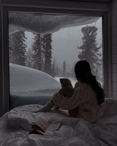 a woman sitting on top of a bed reading a book in front of a window