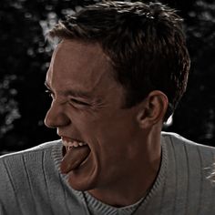 a man laughing with his mouth open in front of him and trees behind him on a dark background