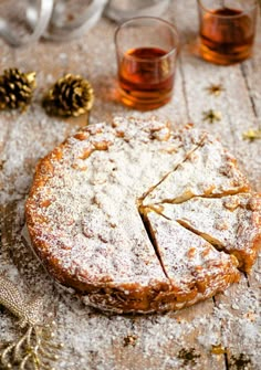 a cake with powdered sugar on it sitting next to two glasses and pine cones