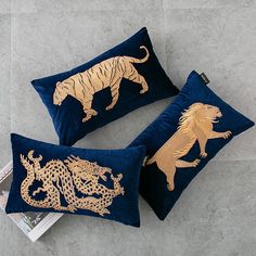 two blue velvet pillows with gold embroidered tiger and lion on them, sitting on the floor