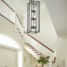 a large foyer with white walls and wood floors, an iron chandelier over the staircase