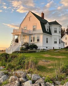 a large white house sitting on top of a lush green field next to the ocean